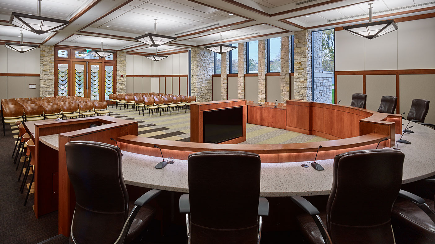 The new council chambers interiors feature stone pier accents, a raised wood dais, coffered ceilings, and prairie-inspired stained glass entry doors.