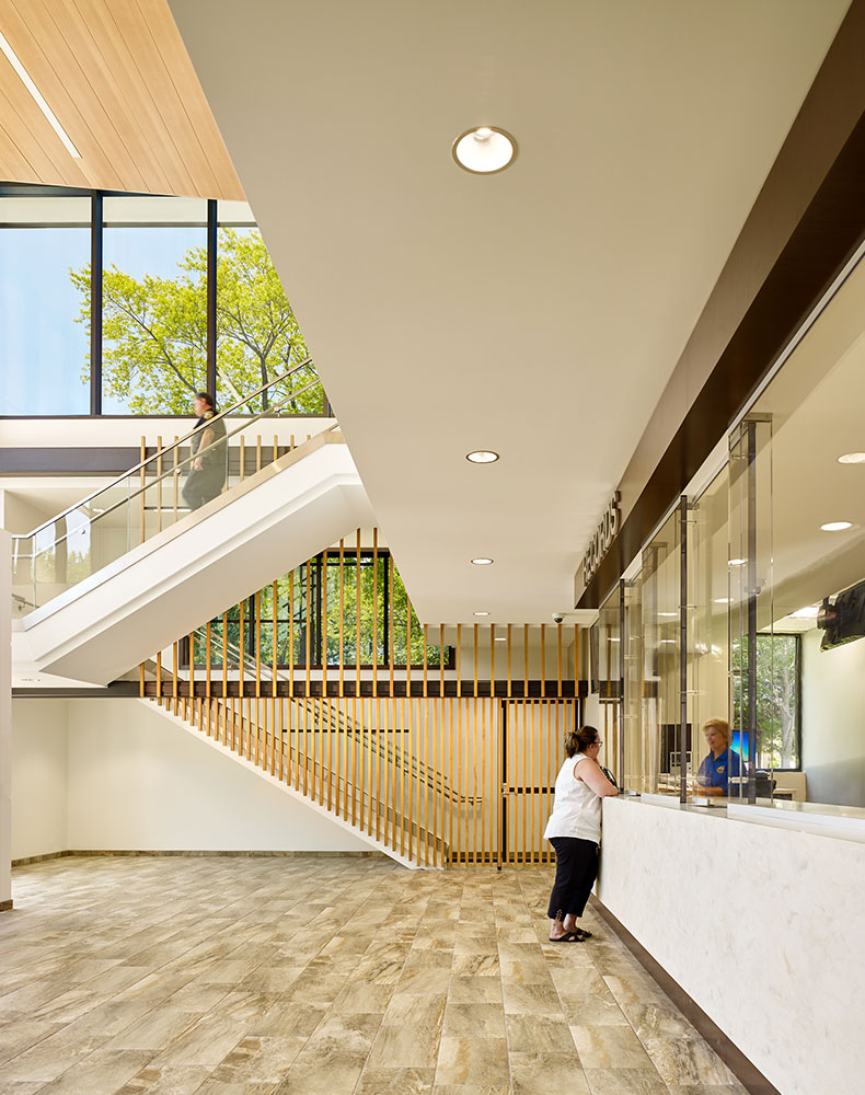 This lobby view features the records counter as well a monumental staircase with vertical wood fins that add visual interest, while acting as an elegant security boundary.