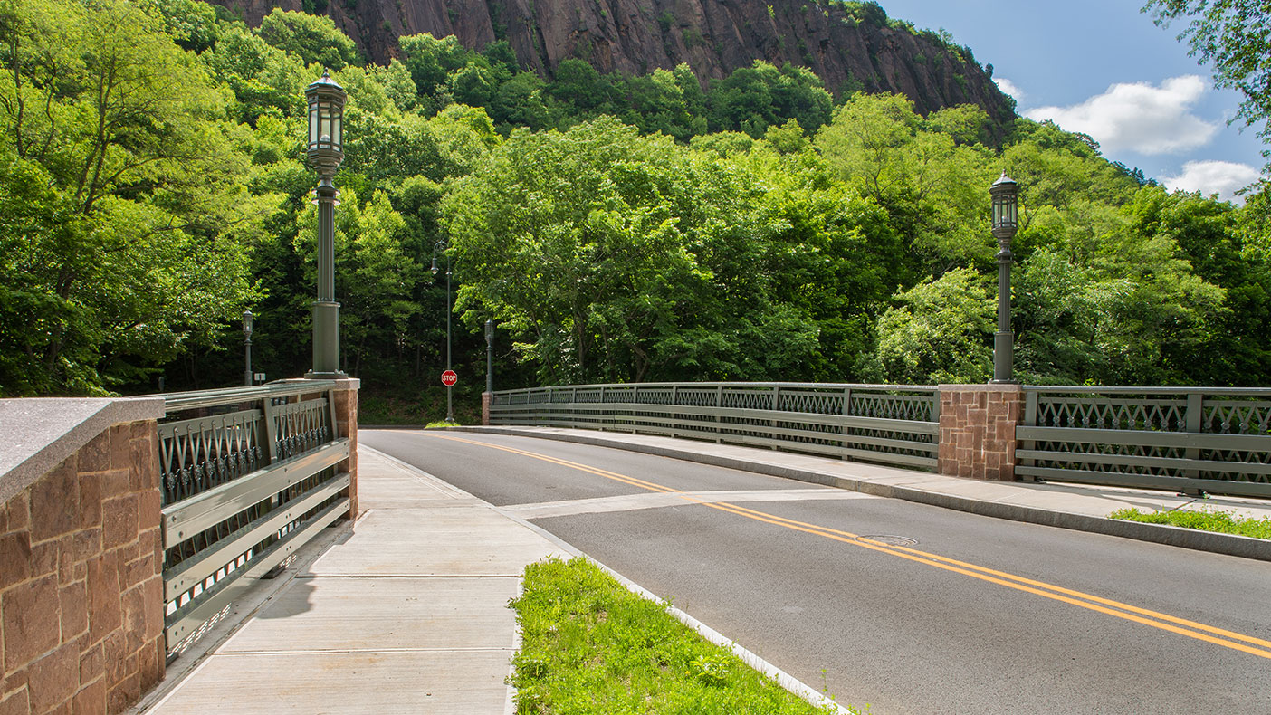 The 84-foot-long single-span steel deck arch bridge carries two lanes of vehicular traffic over a 20-foot roadway and has two five-foot-wide pedestrian sidewalks.